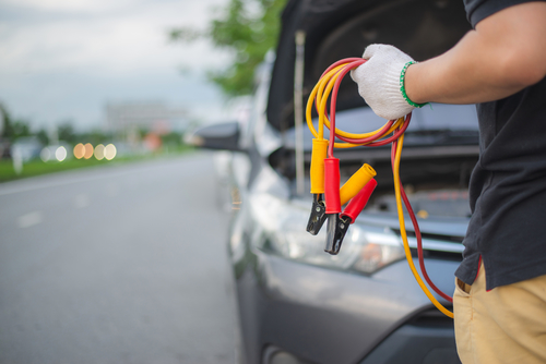 Young man charging battery car with electricity trough jumper cables on the country road,copy space.insurance and service concept.